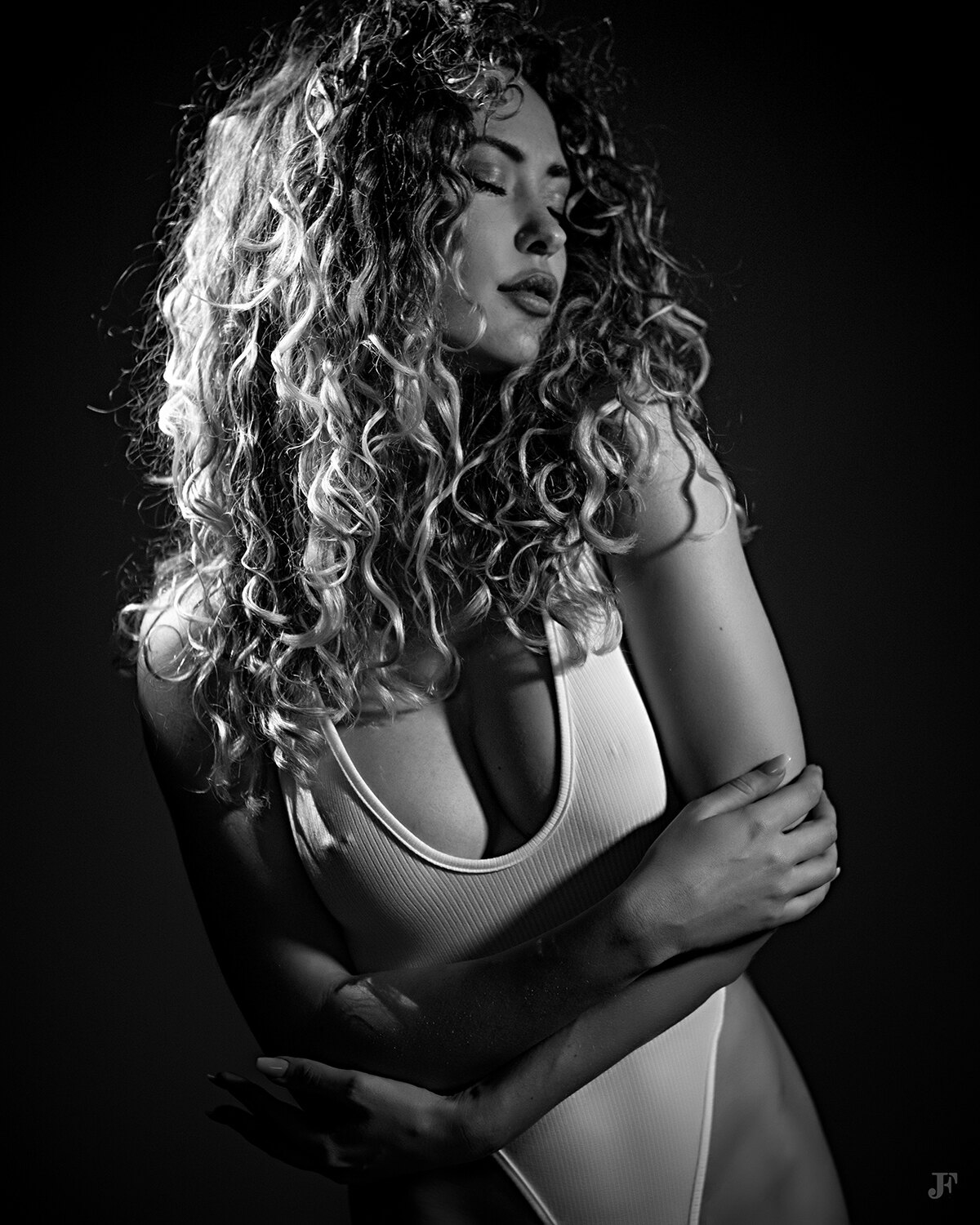 The image shows a woman with long curly hair wearing a white dress against a black background.
