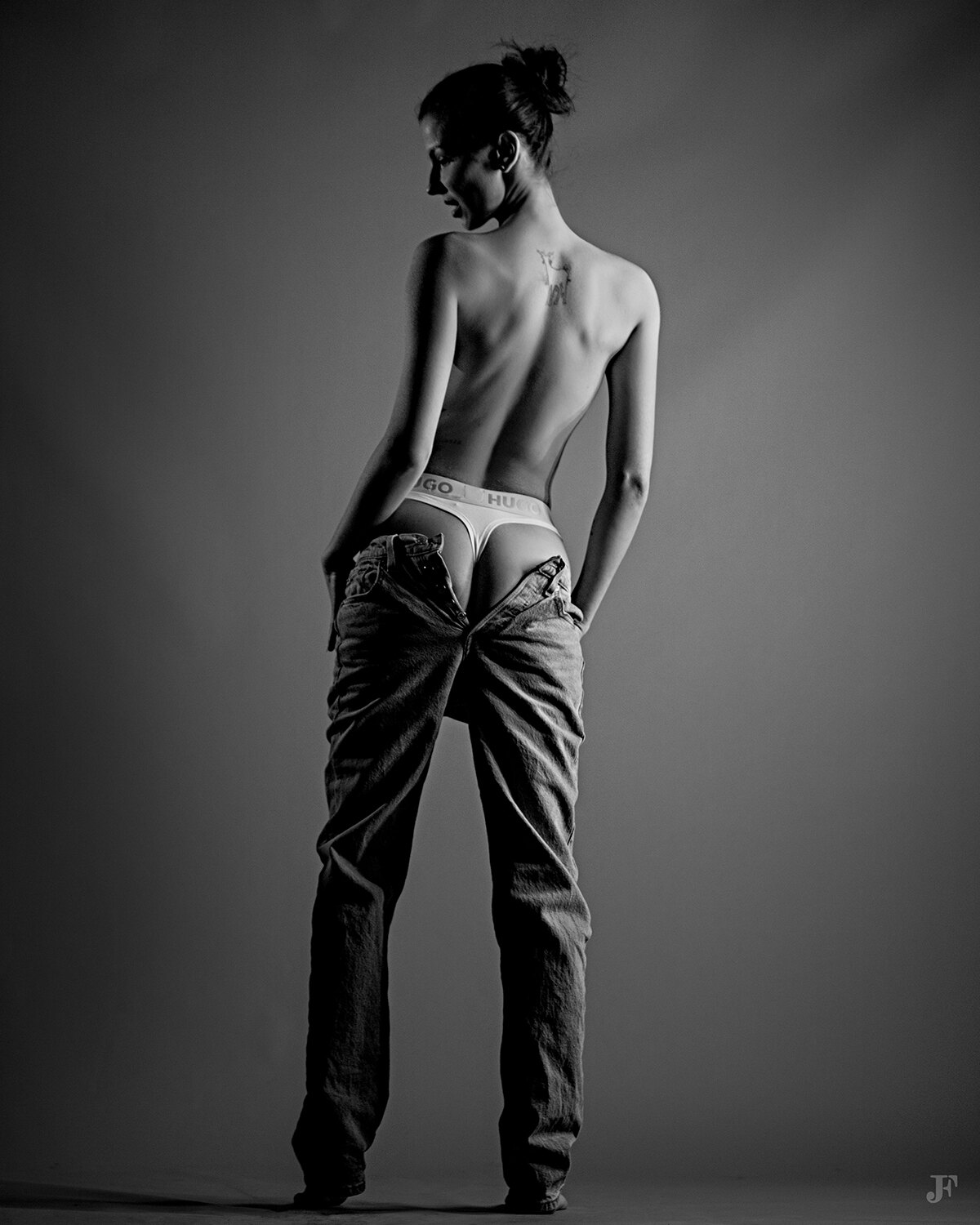 The image shows a woman standing with her back to the camera, wearing a pair of jeans. The image is in black and white, giving it a timeless and classic feel.