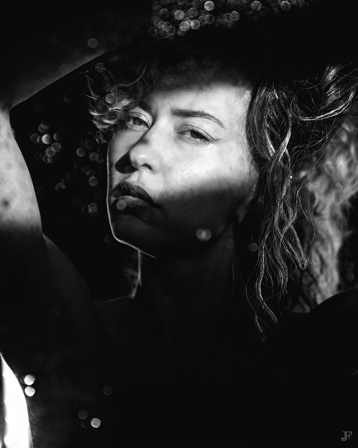 The image shows a black and white photo of a woman wearing a hat. Her face is clearly visible, with her eyes looking directly at the viewer. Her hair is pulled back in a neat bun, and her clothing is simple and minimalistic.