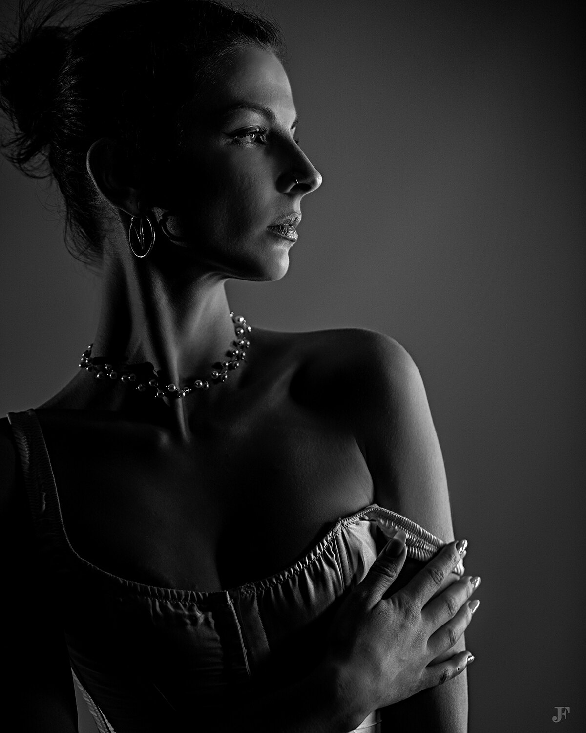 The image shows a woman in a black and white photo wearing a dress and a necklace. She is standing in the center of the image, her posture and expression conveying a sense of confidence and strength. Her dress is simple and elegant, with a high neckline a