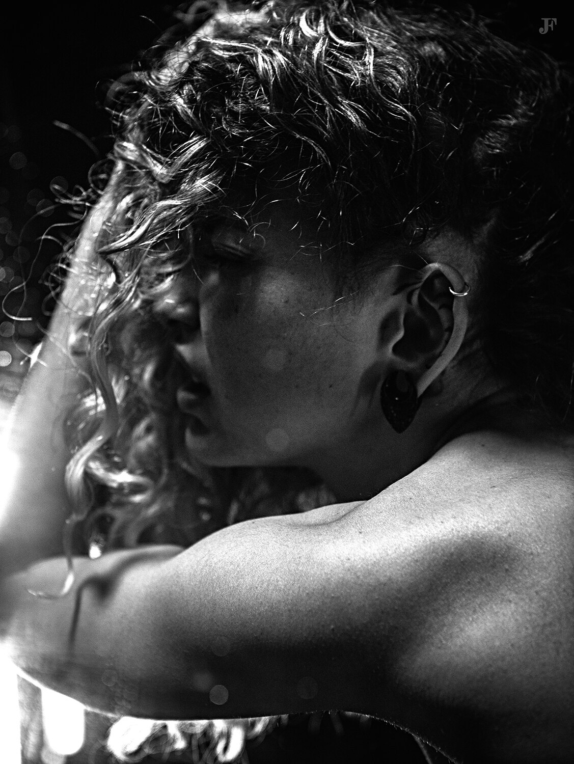 The image shows a woman with curly hair standing in front of a mirror, her face illuminated by the light of the setting sun. She is wearing a black and white outfit, and her hair is cascading down her back.