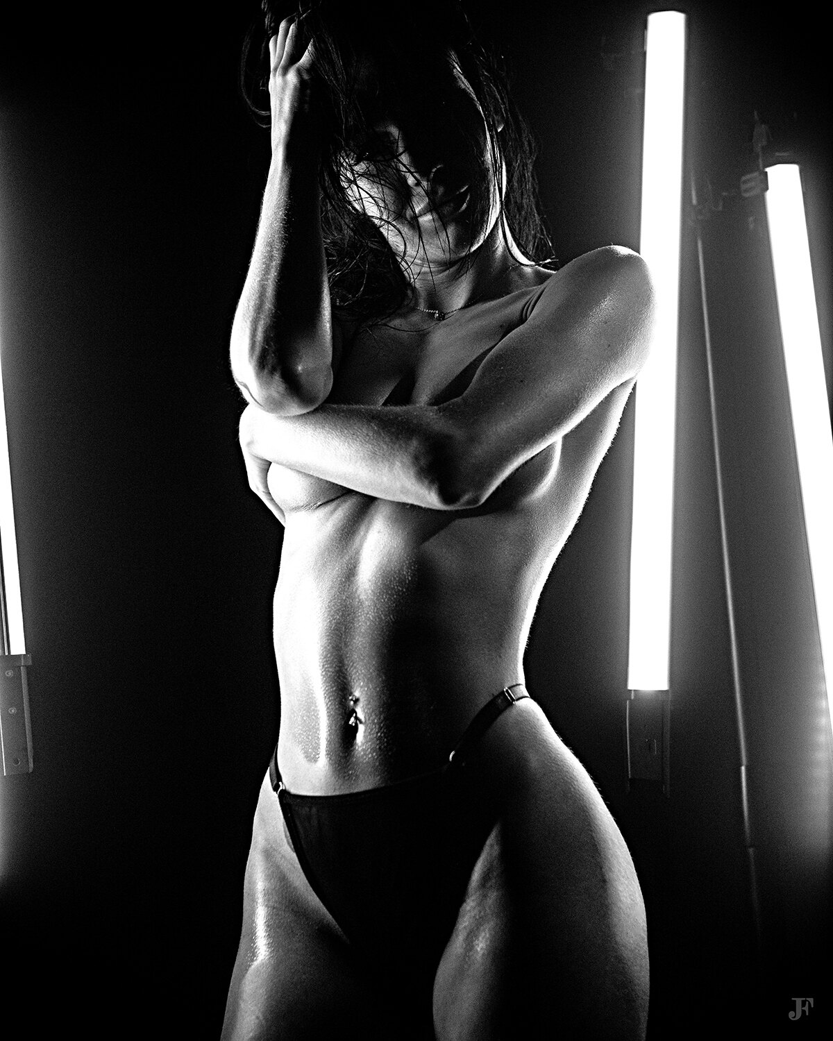 The image shows a black and white photo of a woman in a bikini standing in front of a light, with a dark background.