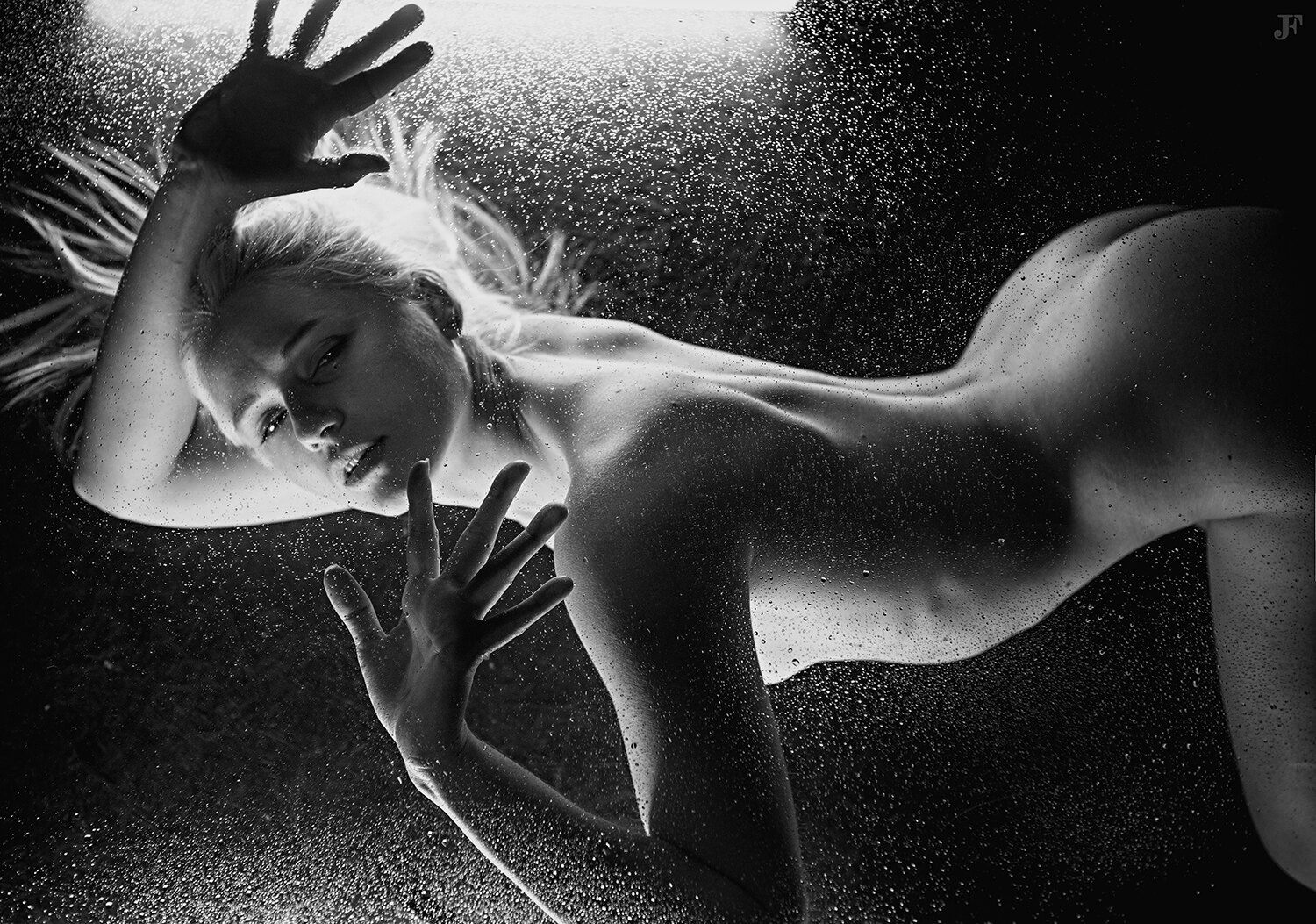 The image shows a black and white photo of a woman laying on the ground with her arms outstretched, surrounded by water droplets.