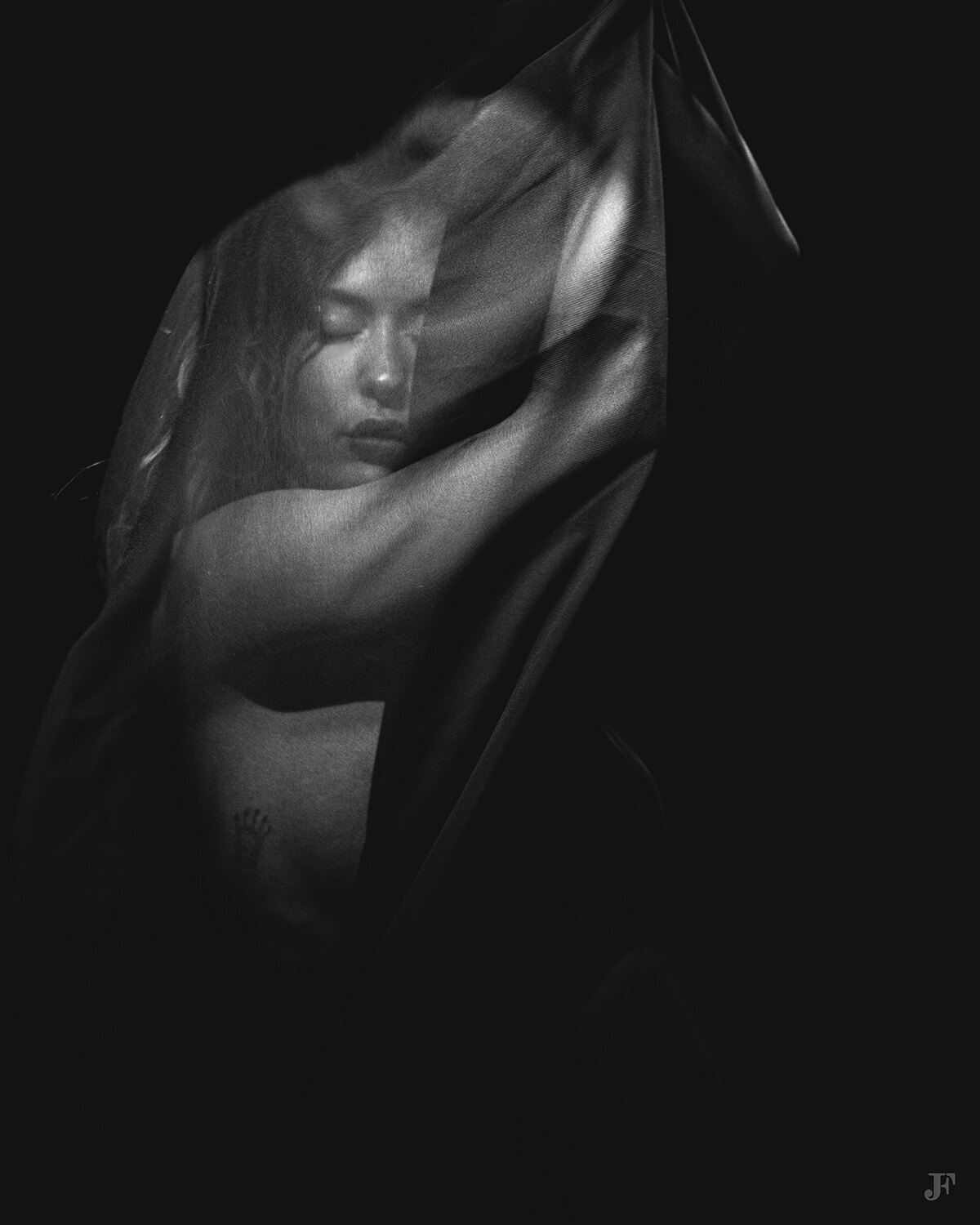 The image shows a black and white photo of a woman with her arms outstretched, her face partially obscured by a cloth. The background is dark, creating a mysterious atmosphere.