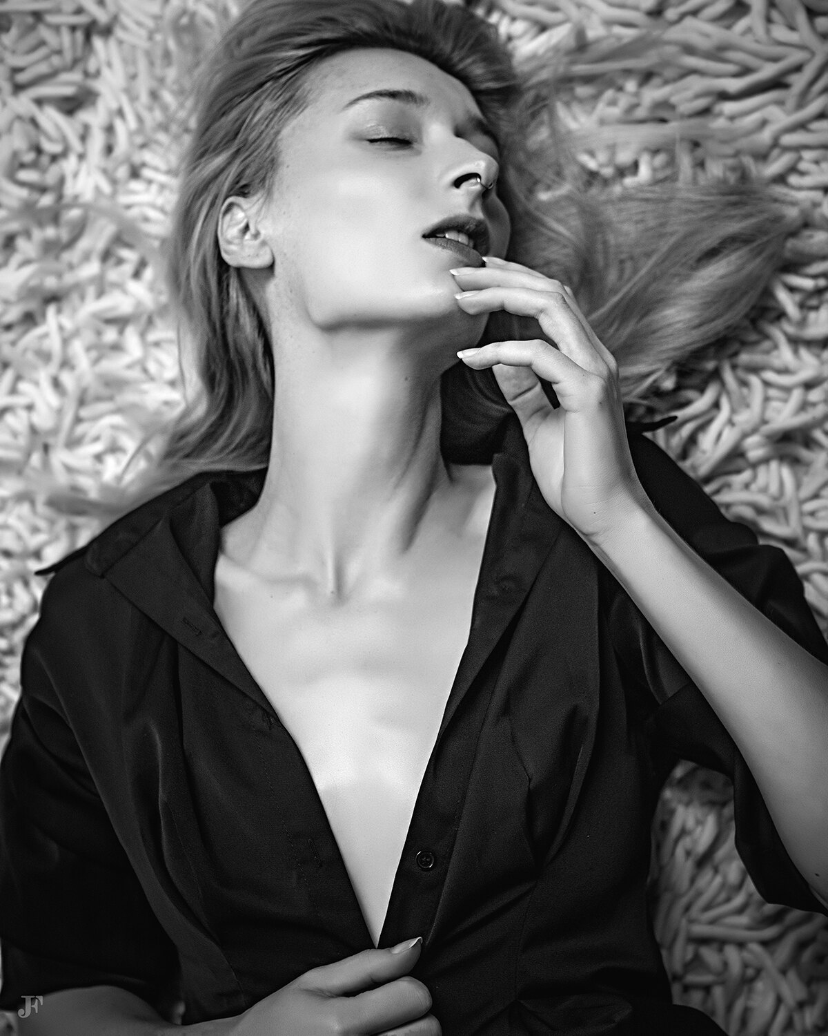 The image shows a woman laying on top of a bed with her hair blowing in the wind, wearing a black dress. The image is in black and white, giving it a timeless and classic feel.