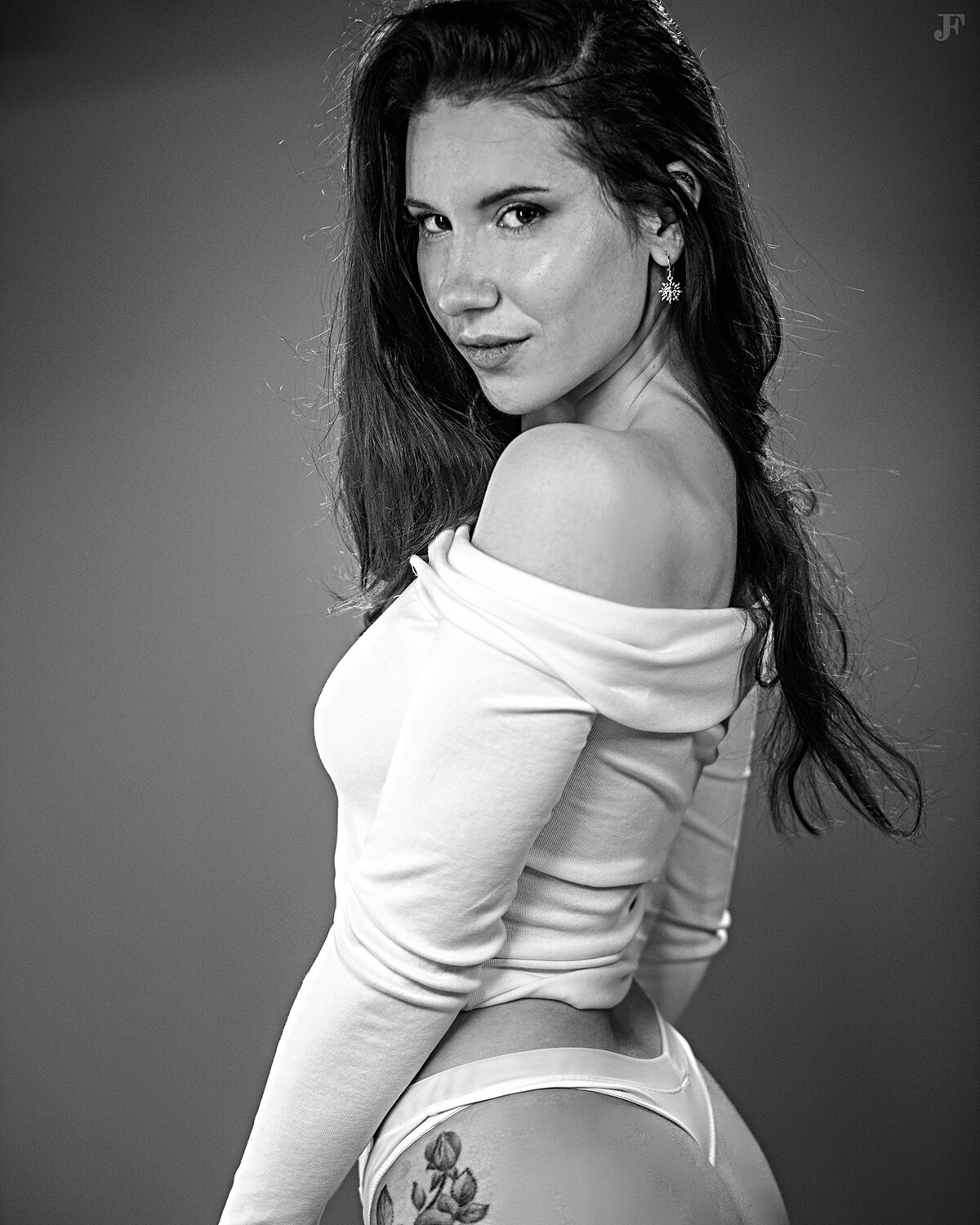 The image shows a woman in a white shirt and panties posing for a black and white photo. She is standing in the center of the image, with a watermark in the top right corner.