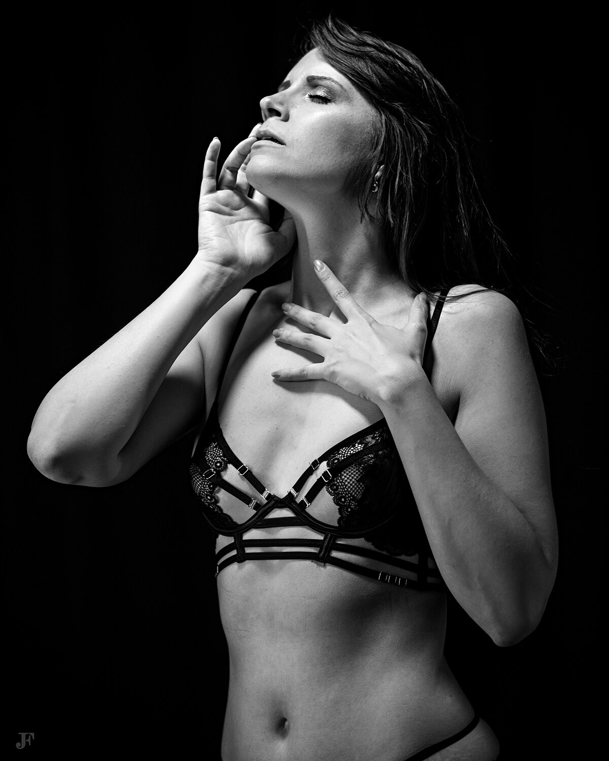 The image shows a woman in a black lingerie posing for a picture against a dark background. She is wearing a bra and panties, and her hair is styled in a sleek bob. Her makeup is subtle and her expression is confident and poised.