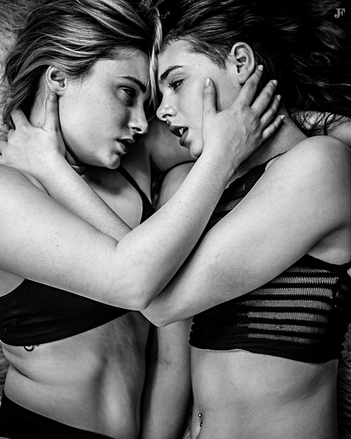 The image shows two young women embracing in a black and white photo. They are both wearing black dresses and appear to be in a loving embrace.