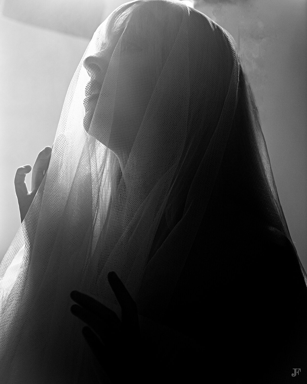 The image shows a woman in a veil standing in front of a window, with a wall in the background. The image is in black and white, giving it a timeless and classic feel.