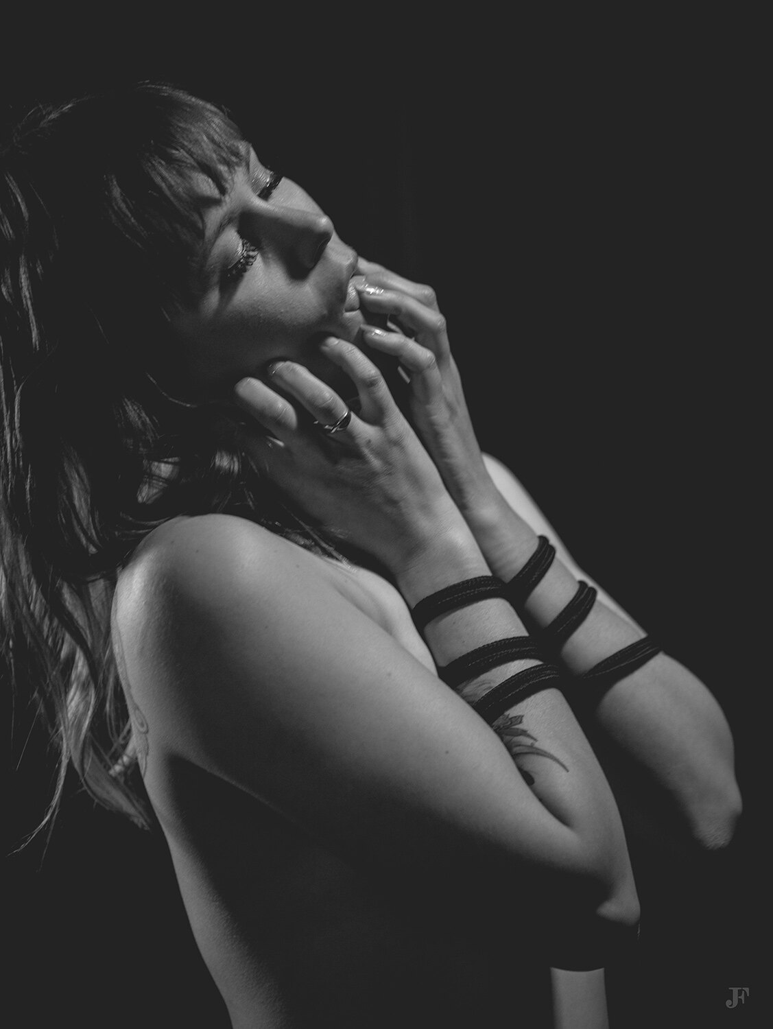 The image shows a black and white photo of a woman with her hand on her chin, standing against a dark background.