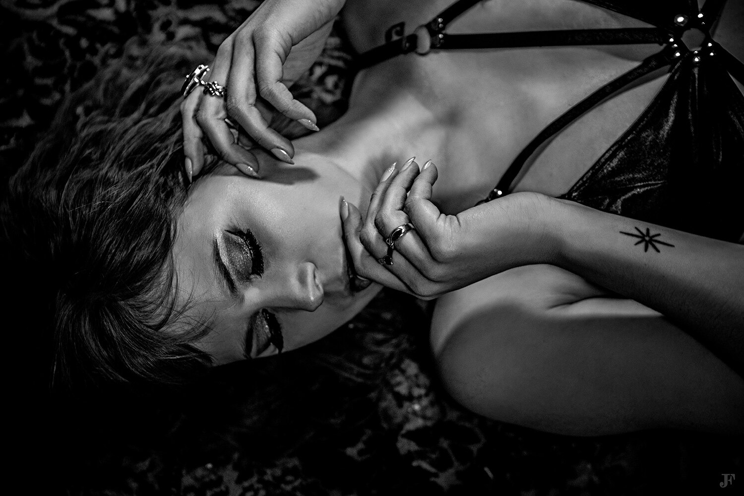 The image shows a woman laying on top of a leopard print blanket in a black and white setting. She is wearing a dress and has a tattoo on her arm.