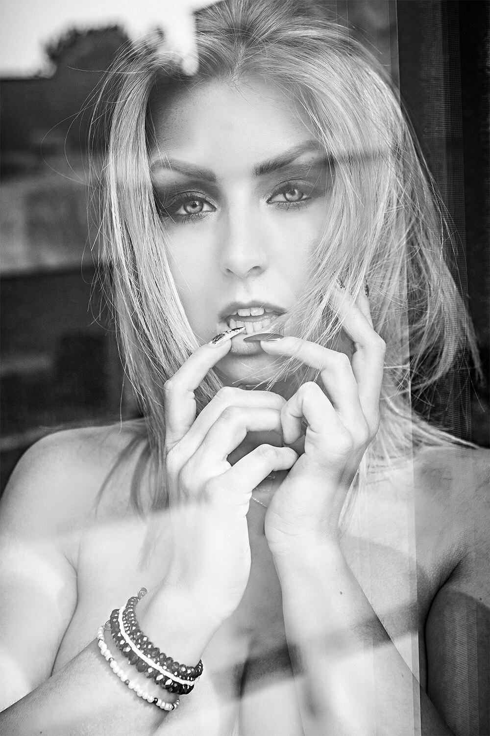 The image shows a black and white photo of a woman with long blonde hair wearing a bracelet. The background is blurred, giving the focus to the woman.